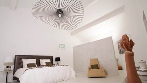 Une chambre moderne avec un grand lit, un fauteuil, un luminaire au plafond original et une sculpture.