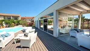 Un espace de vie extérieur moderne, doté d’une piscine, de meubles blancs et de portes vitrées donnant sur un patio abrité.