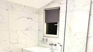 Une salle de bain moderne dotée d’une douche à parois de verre, d’une grande baignoire et d’une fenêtre avec un store.