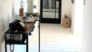 Un couloir avec un miroir à cadre noir, une œuvre d’art encadrée, un téléphone et un sac en tissu tressé.