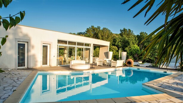 Une maison moderne dotée d’une piscine, d’un espace salon extérieur et d’une grande porte vitrée.