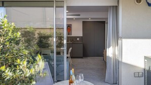 A modern apartment with a glass door leading to a balcony, a dining area with a table and chairs, and a kitchen visible through the door.