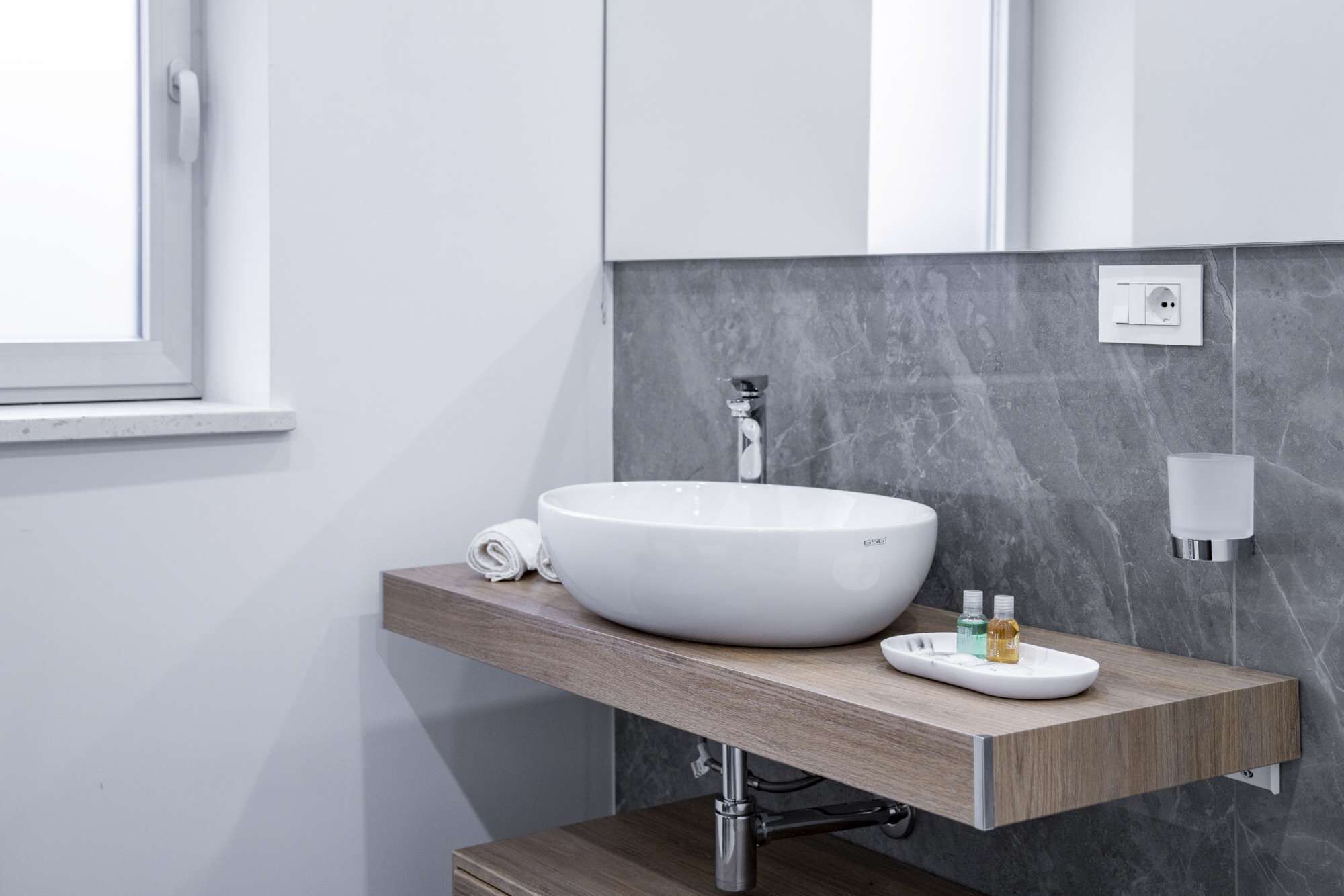 A modern bathroom with a white vessel sink, a wooden vanity, a towel, and a soap dispenser.