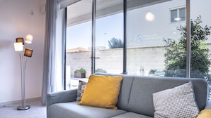 A modern living room with a grey sofa, a yellow pillow, and a patterned pillow. A floor lamp with three shades is visible on the left.