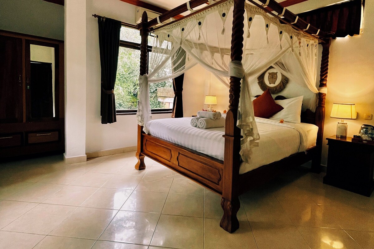 A four-poster bed with a canopy, a ceiling fan, and a nightstand with a lamp.