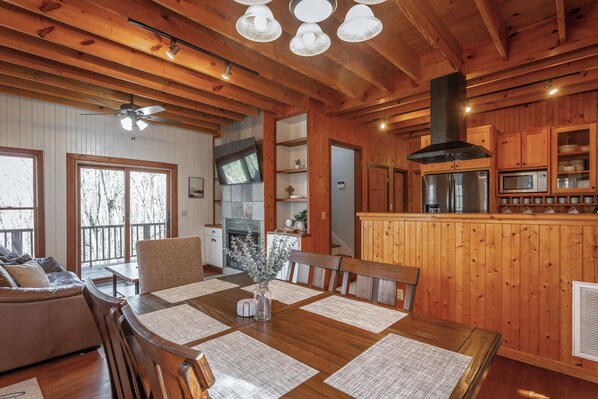 A wooden interior with a dining table, chairs, a sofa, a fireplace, and a kitchen area.