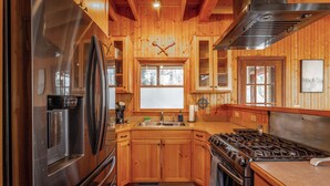 Cocina tipo cabaña de madera con un refrigerador de acero inoxidable, una estufa a gas, gabinetes de madera y un ventanal con vidrio esmerilado.