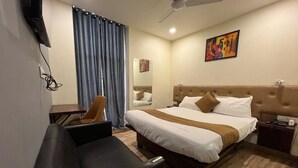 Een hotelkamer met een bed, een bureau, een stoel, een plafondventilator en een schilderij aan de muur.