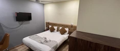 Habitación de hotel ordenada con una cama, una mesita de noche de madera, un televisor montado en la pared y un ventilador de techo.