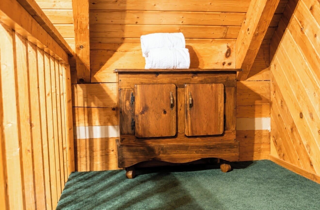 Interior de una cabaña de madera con un armario de madera, una toalla encima y una alfombra verde.