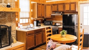 Una cocina con armarios de madera, pared de piedra, chimenea, estufa, microondas, refrigerador y una mesa de comedor con sillas.