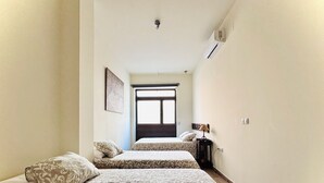 A hotel room with two beds, a window, an air conditioner, and a lamp. - A DIFFERENT SPACE IN TRIANA (Sevilla)