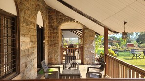 A covered patio area with stone walls, wooden furniture, and a view of a garden. - Madhuvan Retreat Resort Amba (Shahuwadi)