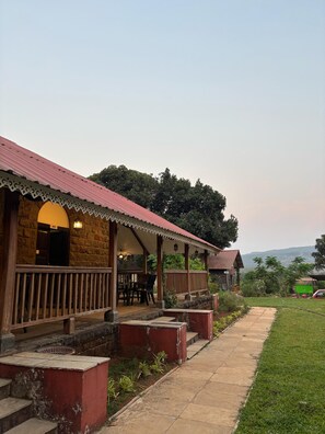 A building with a stone facade, a red roof, and a covered porch with outdoor seating. - Madhuvan Retreat Resort Amba (Shahuwadi)