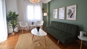 A living room with a green sofa, white chairs, a small table with a lamp, and framed artwork on the wall. - Acropolis Ifigenia Sunny 2 BR, Koukaki, Steps from Landmarks (Athina)