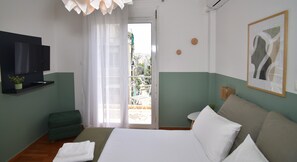 A hotel room with a bed, a TV, a green ottoman, a balcony with a view, and a painting on the wall. - Acropolis Ifigenia Sunny 2 BR, Koukaki, Steps from Landmarks (Athina)