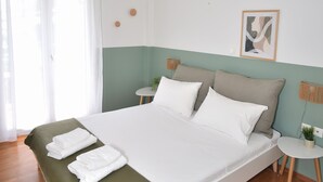 A neatly made bed with white linens and a green throw blanket, a hanging light fixture, a small round table with a plant, and a framed picture on the wall. - Acropolis Ifigenia Sunny 2 BR, Koukaki, Steps from Landmarks (Athina)