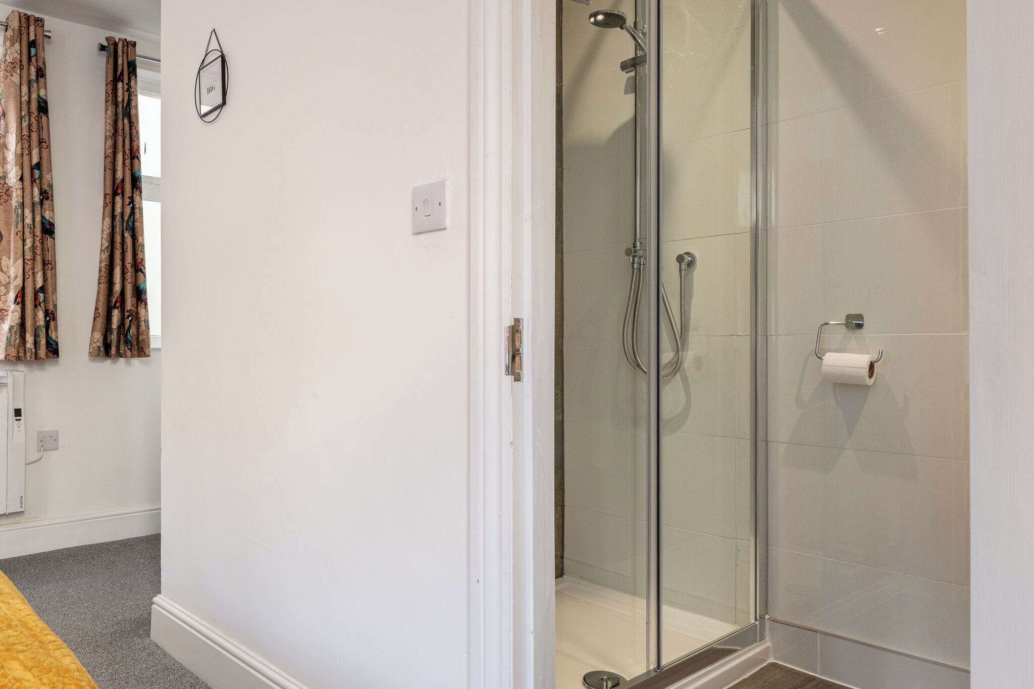 Een moderne badkamer met een douchecabine van glas, een toiletrolhouder en een stopcontact op de muur.