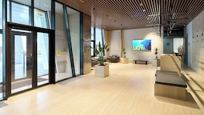 Un hall d’entrée moderne avec des portes en verre, un plancher en bois et un espace détente équipé d’un écran de télévision.