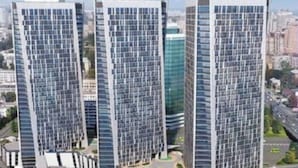 Un immeuble moderne de grande hauteur, doté d’une façade à motifs géométriques, entouré de verdure et bordé par une rue très fréquentée.