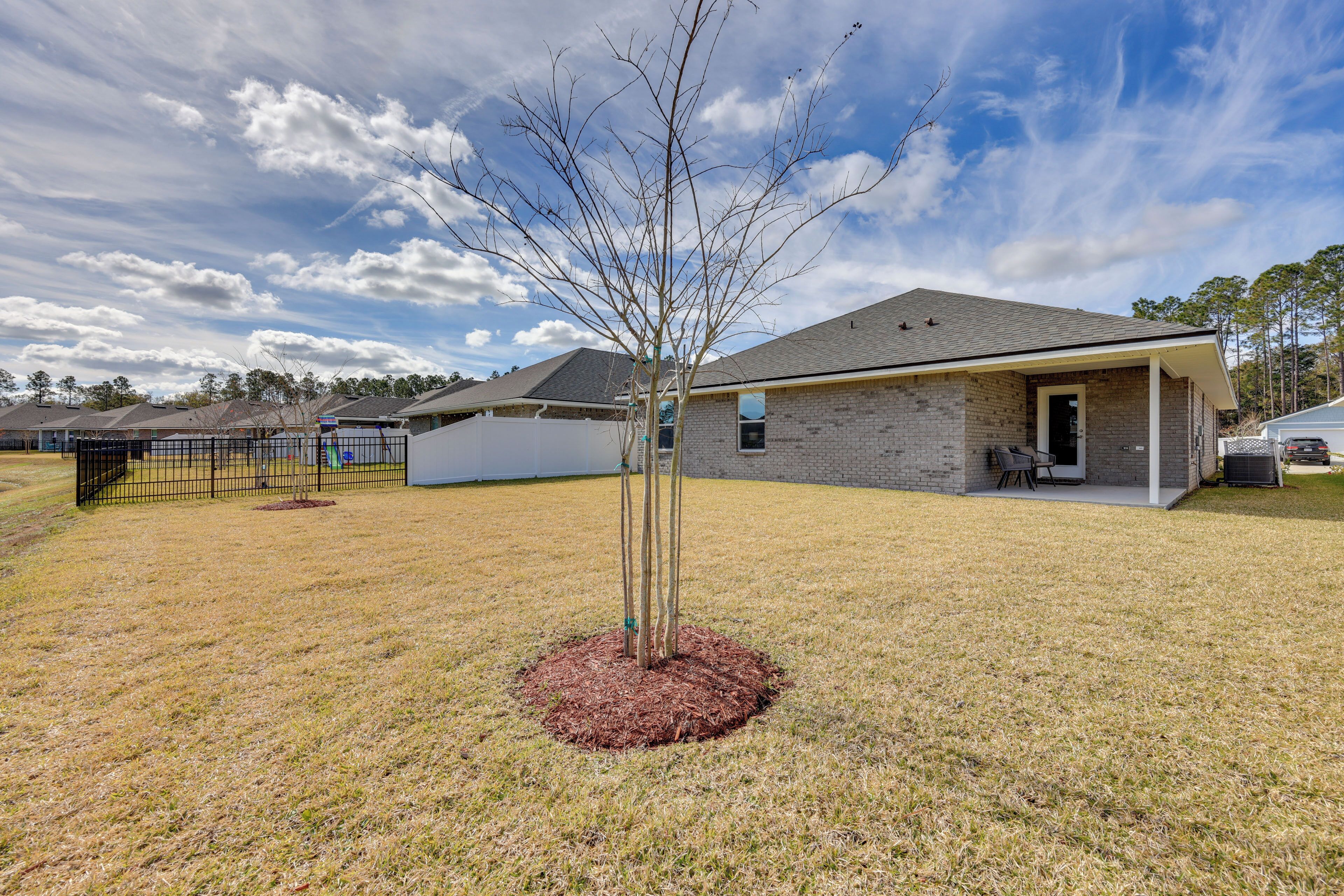 A residential building with a brick exterior, a covered patio, and a small tree in the front yard.