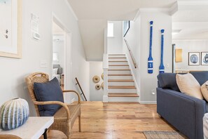 Un salon avec un escalier, un plancher en bois et un canapé bleu.