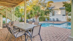 An outdoor patio with a pool, wooden pergola, and lounge chairs.