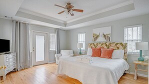 A bedroom with a bed, a television, a ceiling fan, and a window with blinds.