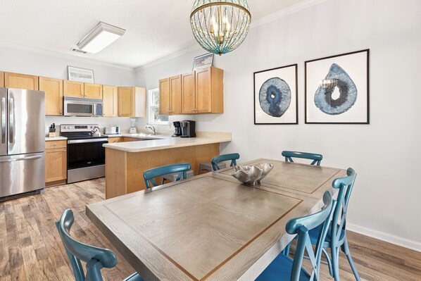 Una cocina moderna con armarios de madera, electrodomésticos de acero inoxidable y un comedor con mesa de madera y sillas azules.
