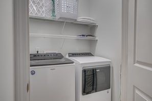 Un cuarto de lavandería con lavadora y secadora Whirlpool, un estante con cestos de ropa y un enchufe.