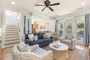 Un salon spacieux avec un canapé bleu, deux fauteuils, une table basse et un ventilateur de plafond.