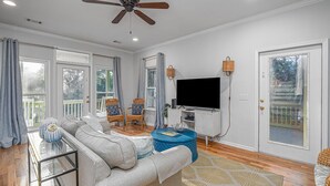 A spacious living room with a large sofa, a television, wicker chairs, and a ceiling fan.