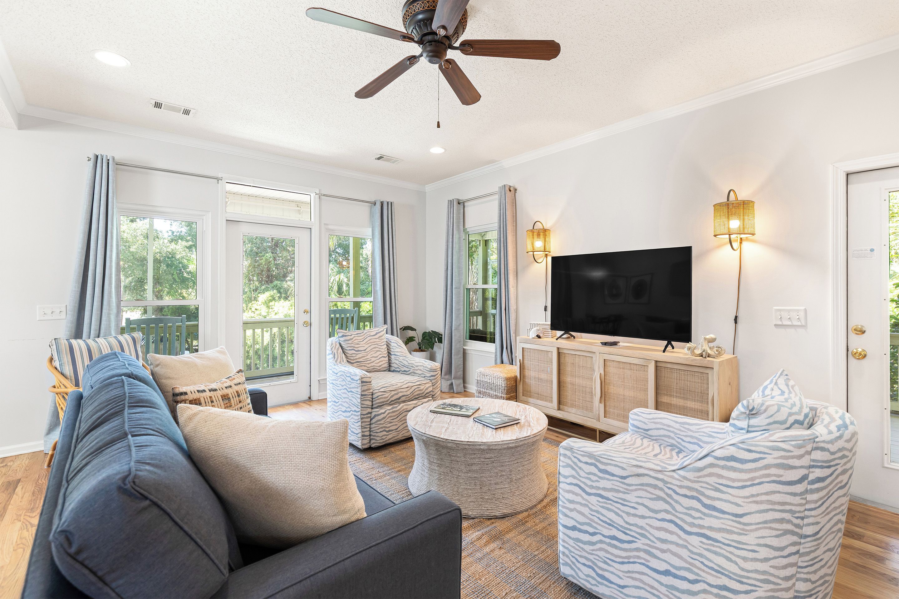 Ein geräumiges Wohnzimmer mit Deckenventilator, großen Fenstern, einem Flachbildfernseher und einer gemütlichen Sitzecke.