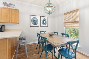 Un coin repas avec une table en bois, des chaises bleues, un lustre et des œuvres d’art accrochées au mur.