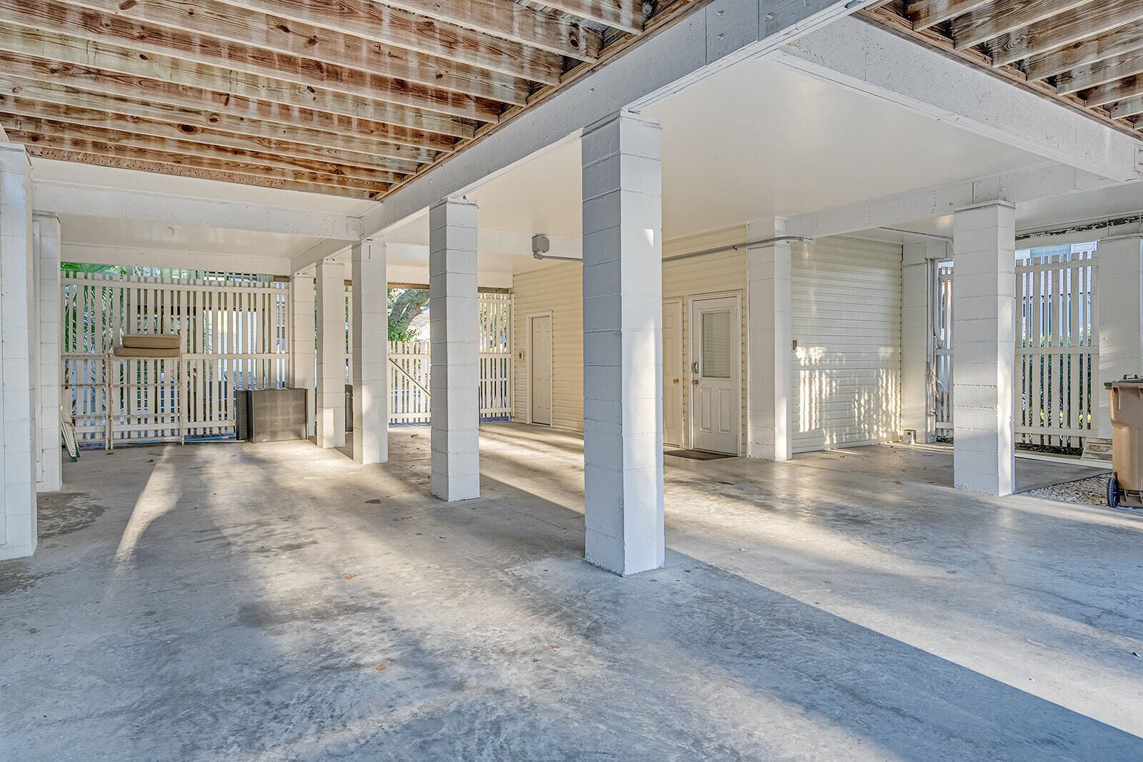 A spacious indoor area with concrete flooring, white pillars, and a high ceiling with exposed wooden beams.