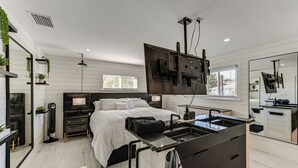 Ein modernes Schlafzimmer mit Bett, Nachttisch, Lampe und einem integrierten Fernseher.
