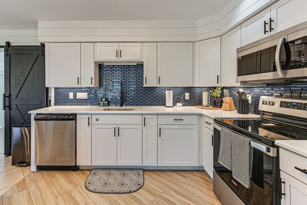 A modern kitchen with white cabinets, a stainless steel dishwasher, a built-in oven, and a microwave. - 1 Mi to Bonita Beach Park: Chic Canal-front Home! (Bonita Springs)