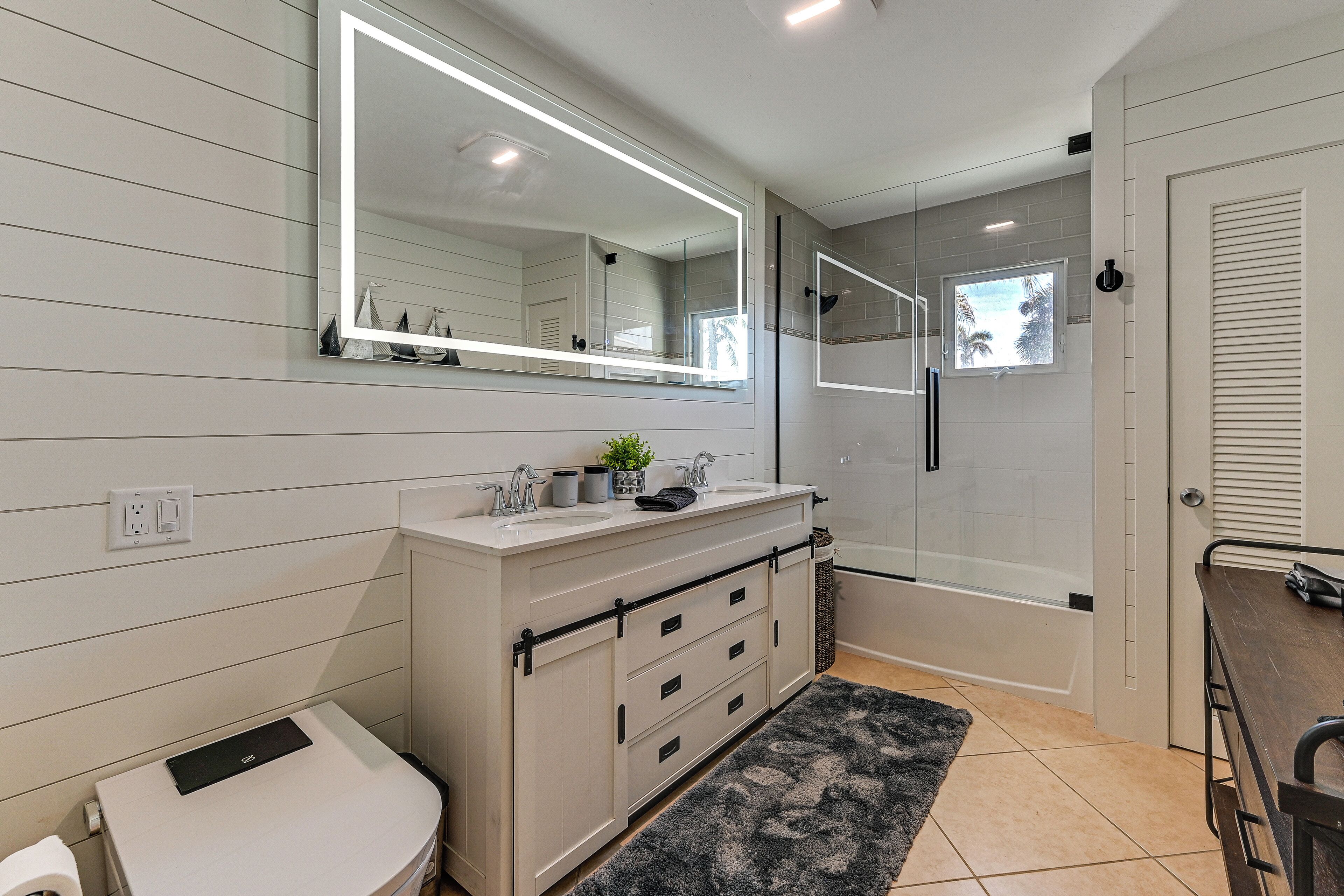 A modern bathroom with a large mirror, two sinks, a shower, and a toilet.
