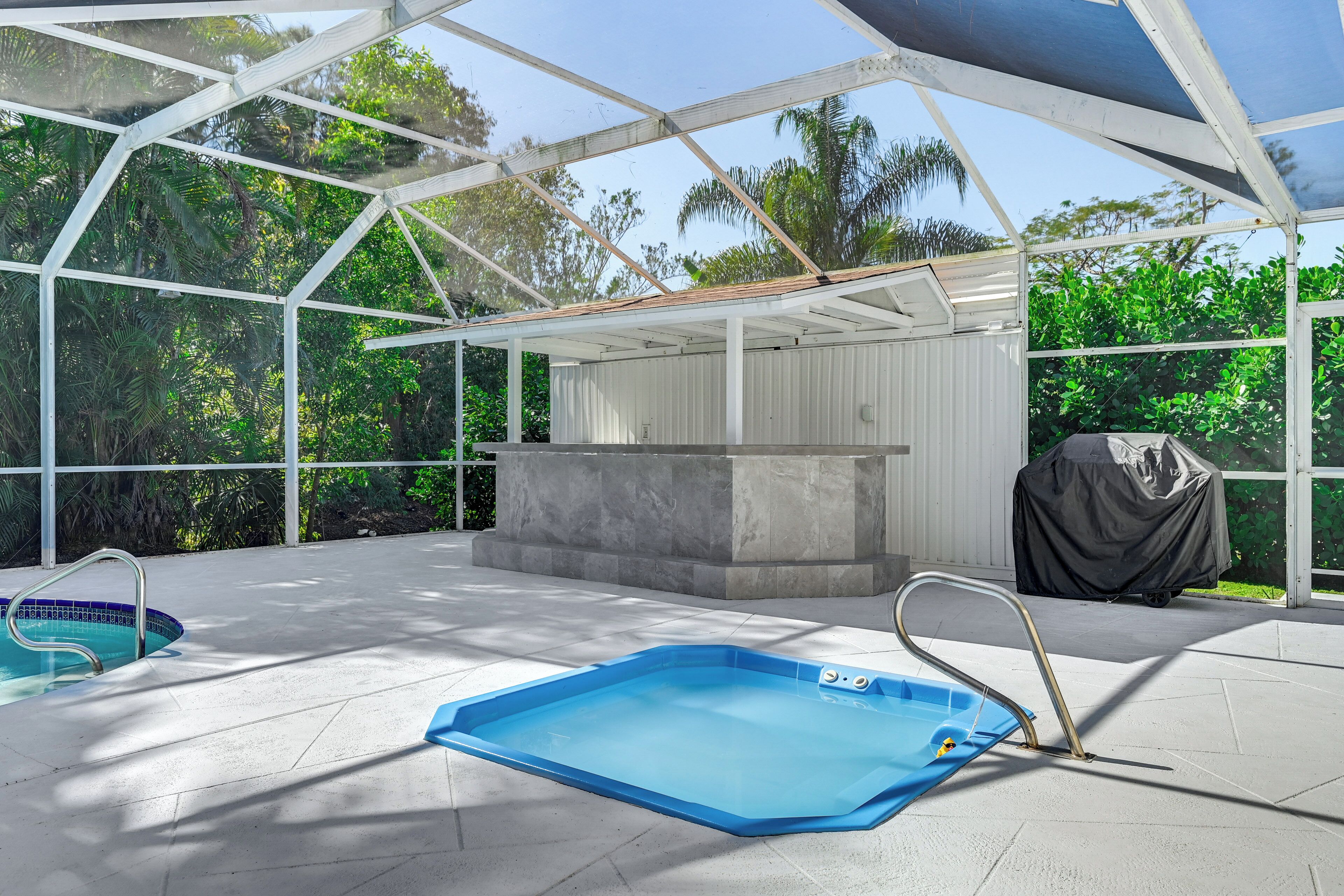 A covered outdoor swimming pool area with a stone bench and a grill.
