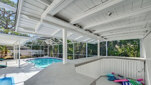 A covered outdoor swimming pool area with a concrete deck, a pool, and various pool toys.
