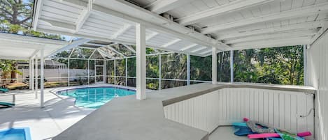 A covered outdoor swimming pool area with a concrete deck, a pool, and various pool toys.