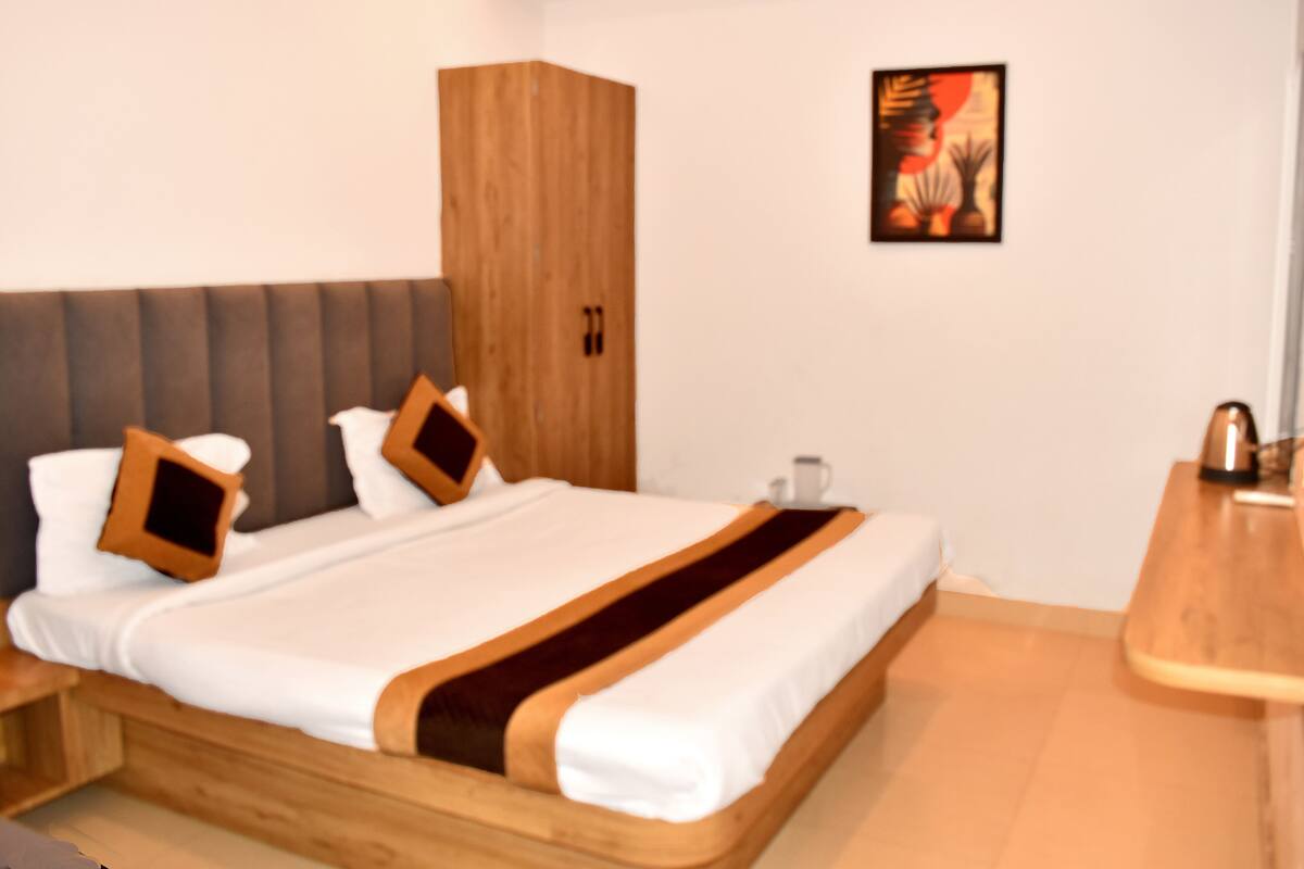 Un dormitorio moderno con un cabecero tapizado gris, una cama con estructura de madera y ropa de cama blanca con detalles marrones.