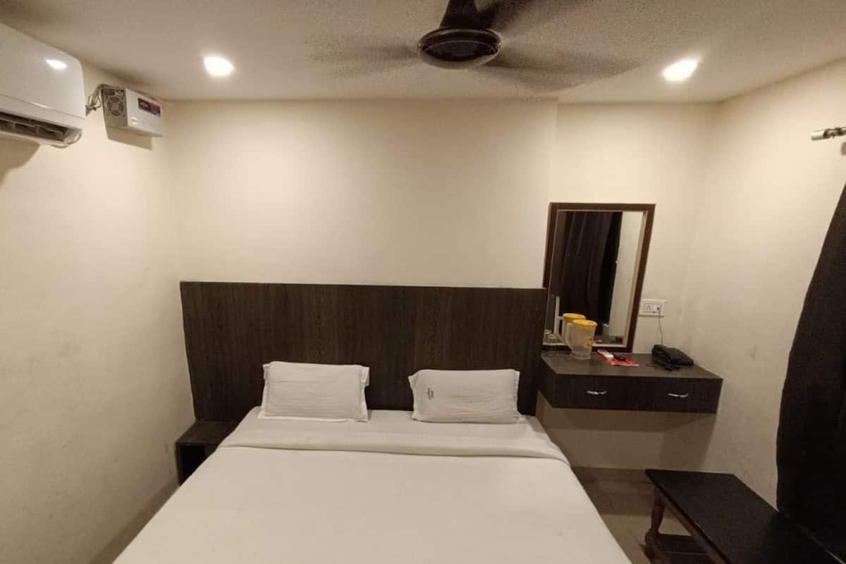 Una habitación de hotel con una cama, una mesita de noche, un espejo y un escritorio con teléfono.