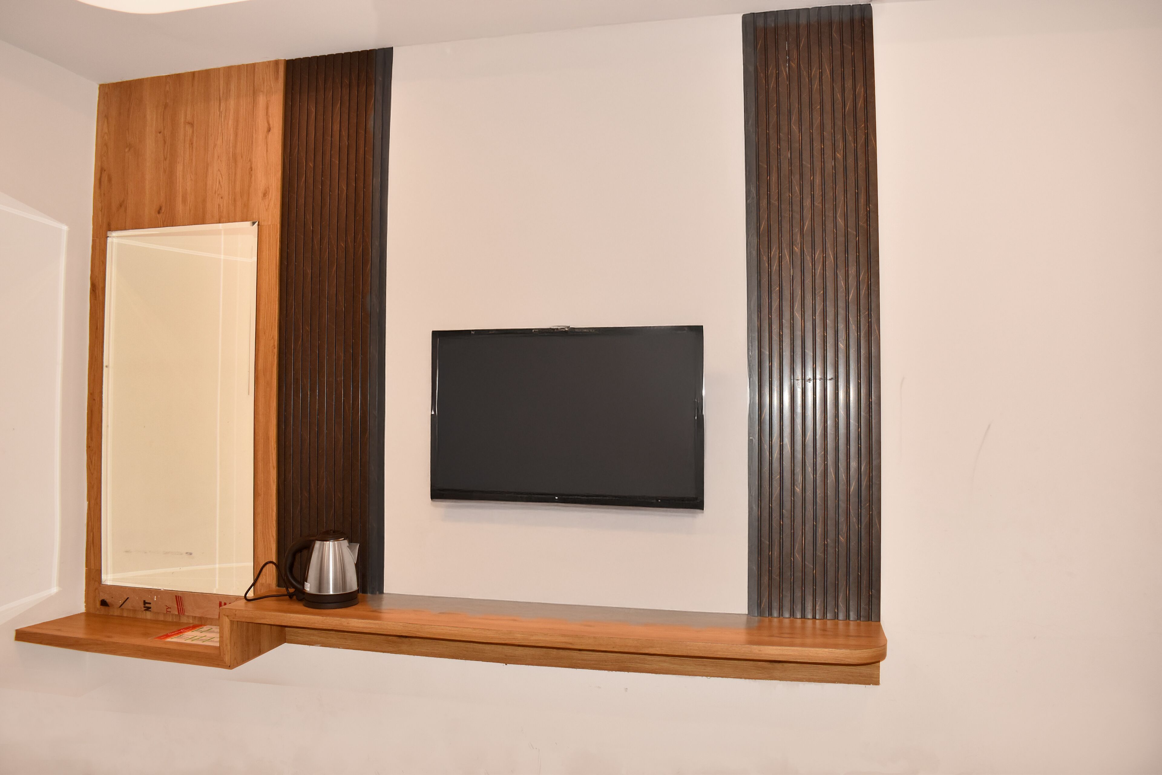 A flat-screen TV mounted on a wall with a wooden shelf below.