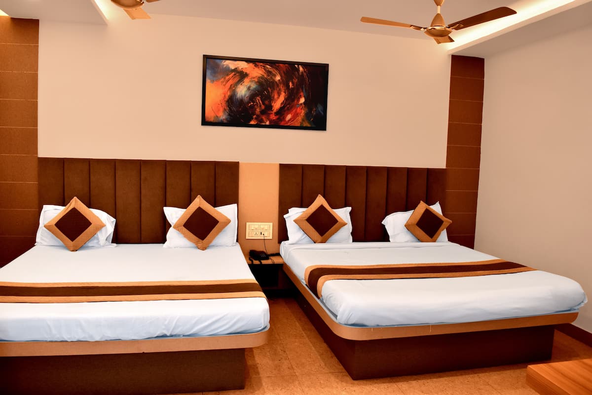 Habitación de hotel con dos camas, cada una con cabecera de madera y ropa de cama blanca. Cuenta con un ventilador de techo, una obra de arte colgada en la pared y una mesita de noche con teléfono.