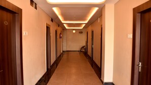 Un couloir d’hôtel avec des portes en bois, des panneaux indiquant le numéro des chambres et un sol carrelé.