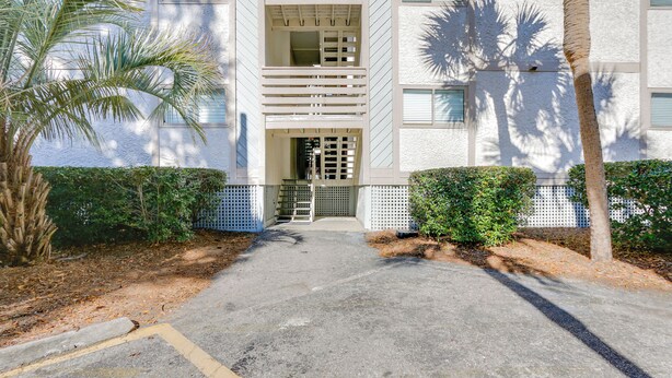 A building entrance with a gated driveway, palm trees, and a white exterior. - < 1 Mi to Coligny Beach Park: Condo w/ Tennis! (Hilton Head Island)