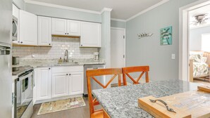 A kitchen with white cabinets, a granite countertop, and a wooden dining table. - < 1 Mi to Coligny Beach Park: Condo w/ Tennis! (Hilton Head Island)