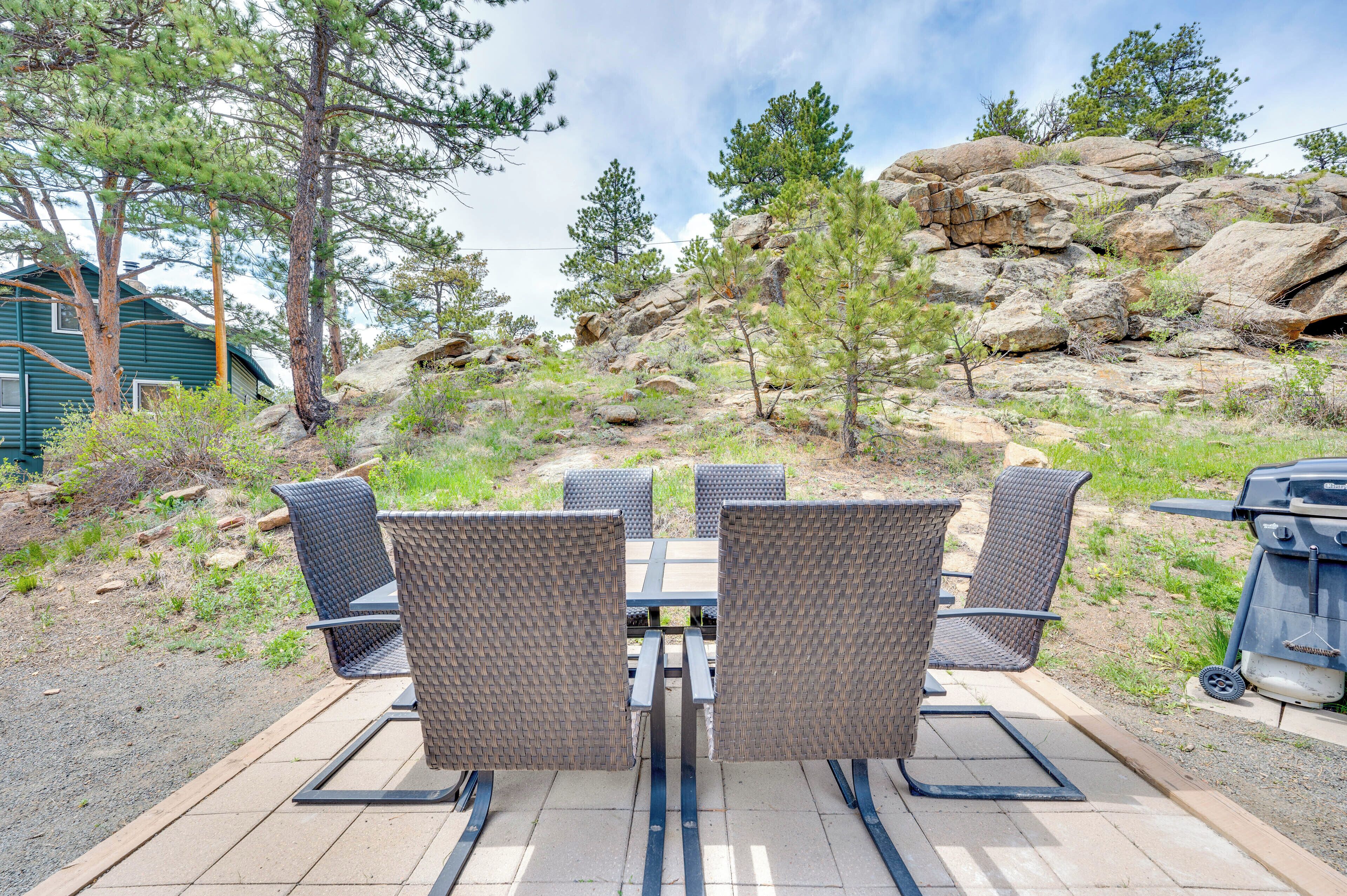 Un patio al aire libre con una mesa y cuatro sillas, rodeado de paisajes naturales con árboles y rocas.