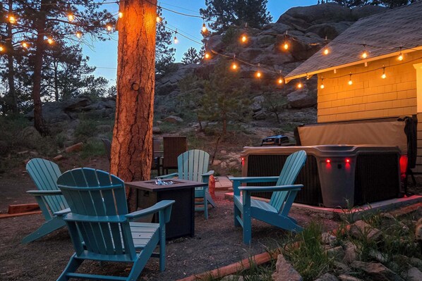 An outdoor seating area with Adirondack chairs, a fire pit, and string lights. - Steps to Estes Lake: Mtn-view Hideaway w/ Hot Tub! (Estes Park)